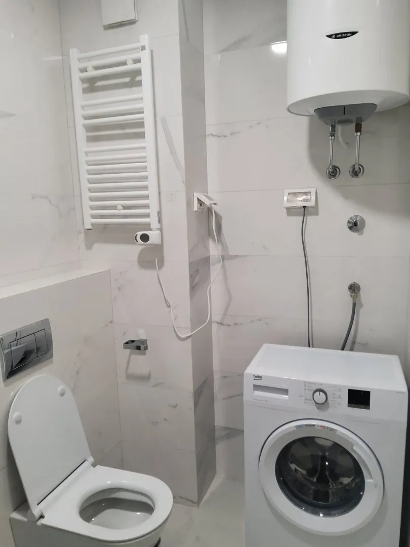 A bright bathroom featuring a washing machine, water heater, and toilet.