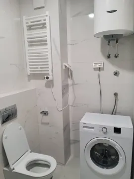 A bright bathroom featuring a washing machine, water heater, and toilet. - image 8