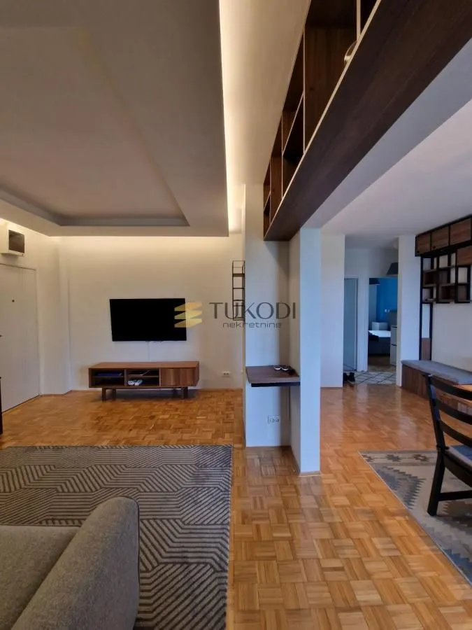 Living room with wooden flooring, a wall-mounted TV, and a dining area.
