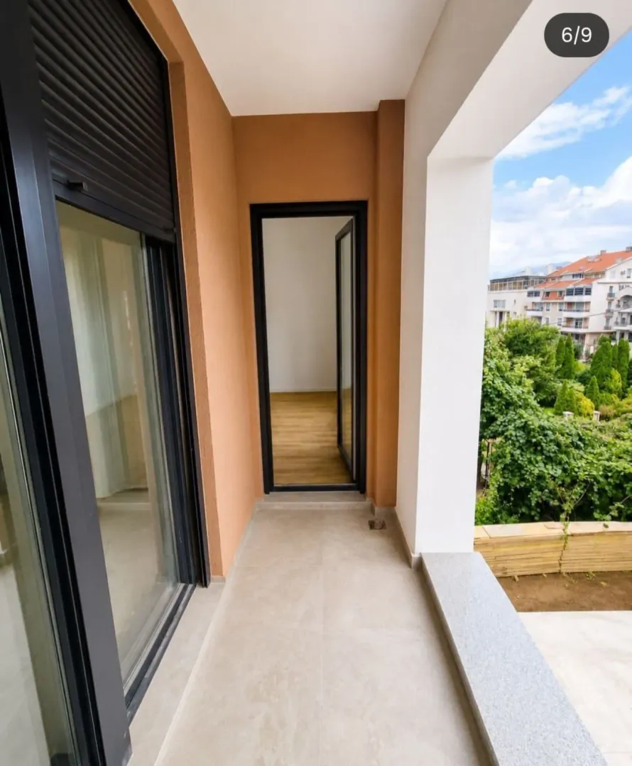 Natkriveni balkon sa keramičkim pločicama i pogledom na zelenilo i okolne zgrade.