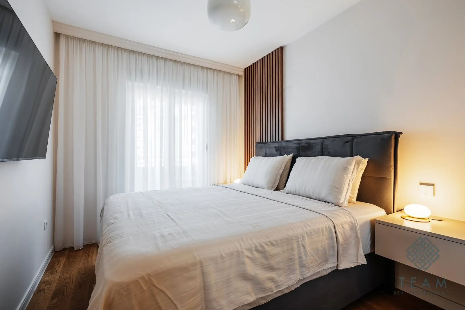 Modern bedroom featuring a double bed, wooden wall panel, and a wall-mounted TV.