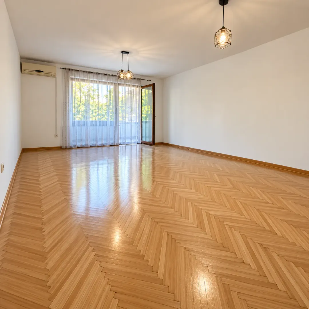 Empty living room with wooden parquet flooring and balcony access.
