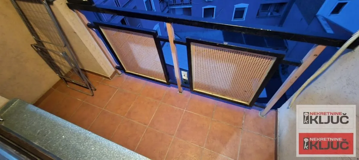 Manji popločani balkon sa metalnom ogradom i pogledom na zgradu.
