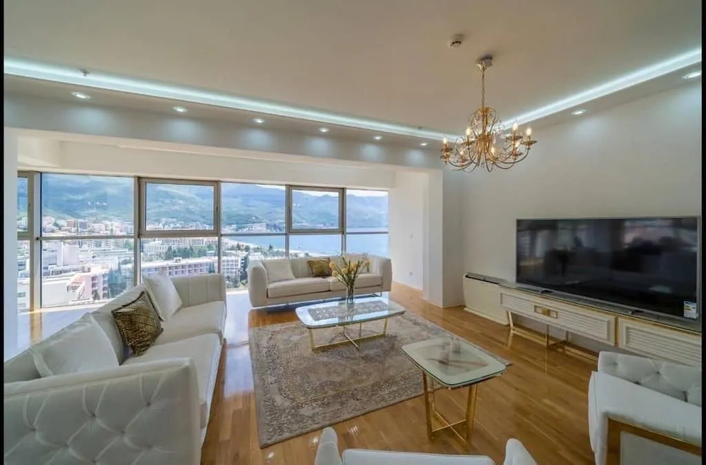 Spacious living room with a sofa set, large TV, and sea views through panoramic windows.