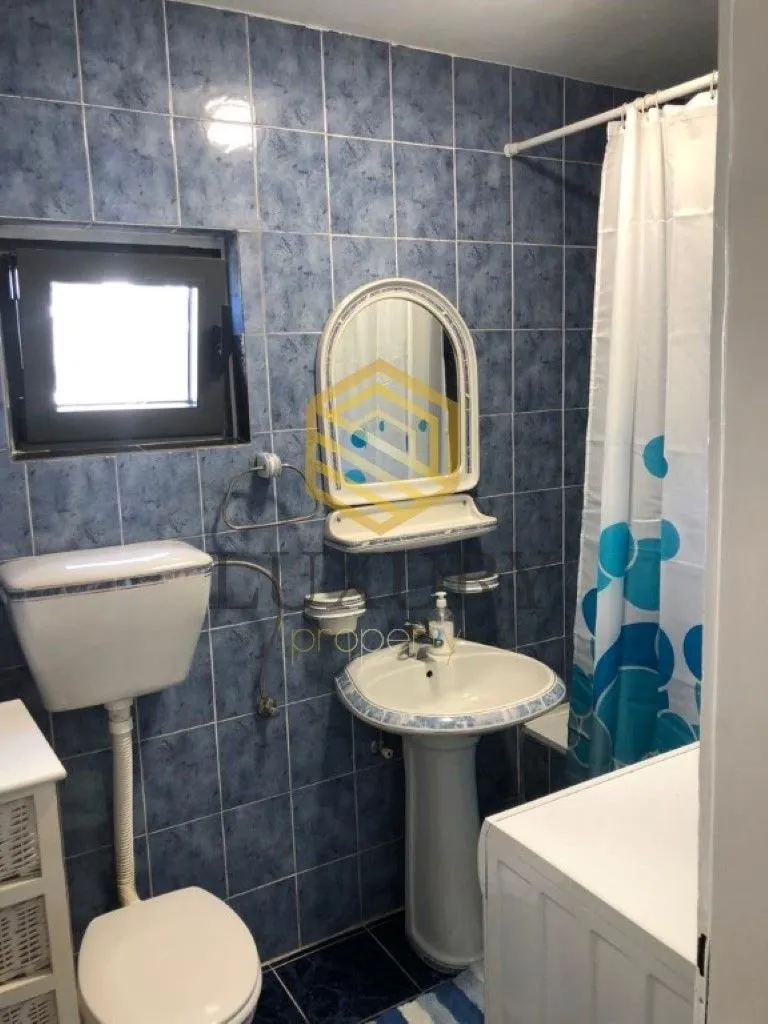 Kupatilo sa plavim pločicama, umivaonikom, ogledalom i toaletom.