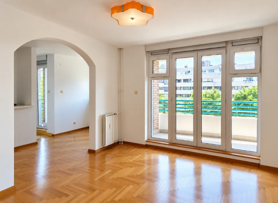 Empty living room with parquet flooring and balcony doors.