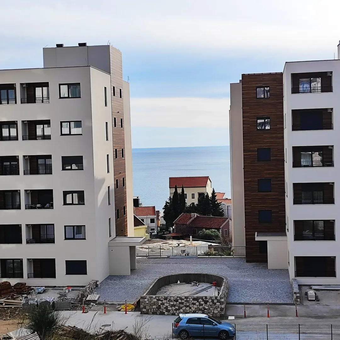 Pogled na zgrade i more između njih sa uređenim dvorištem u prvom planu.