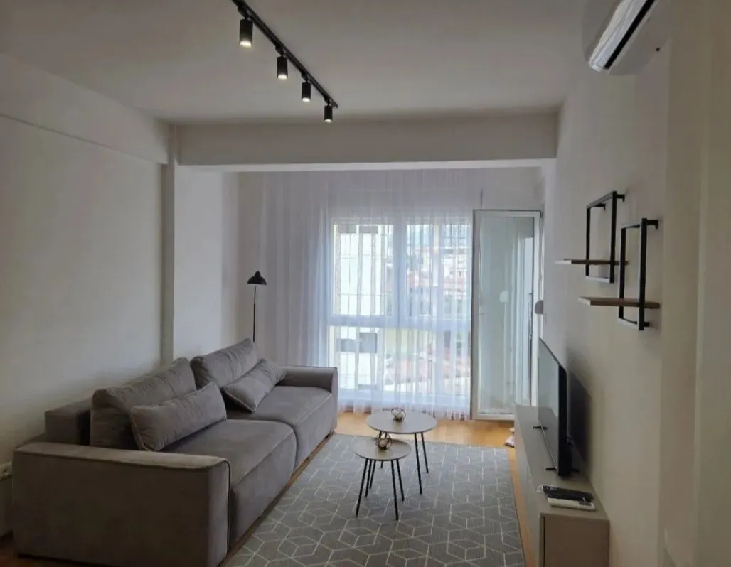 Modern living room with a grey sofa, small coffee tables, and a TV.