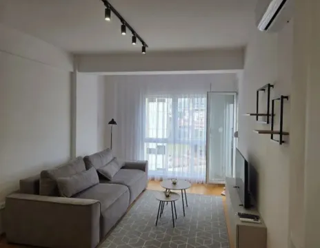 Modern living room with a grey sofa, small coffee tables, and a TV. - image 4