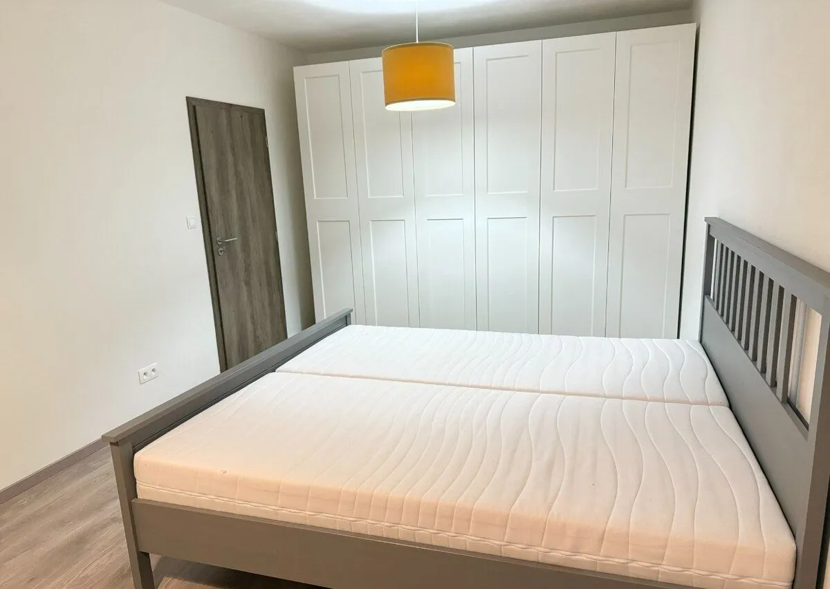 Svijetla spavaća soba sa velikim bračnim krevetom, bijelim garderoberom i drvenim vratima.