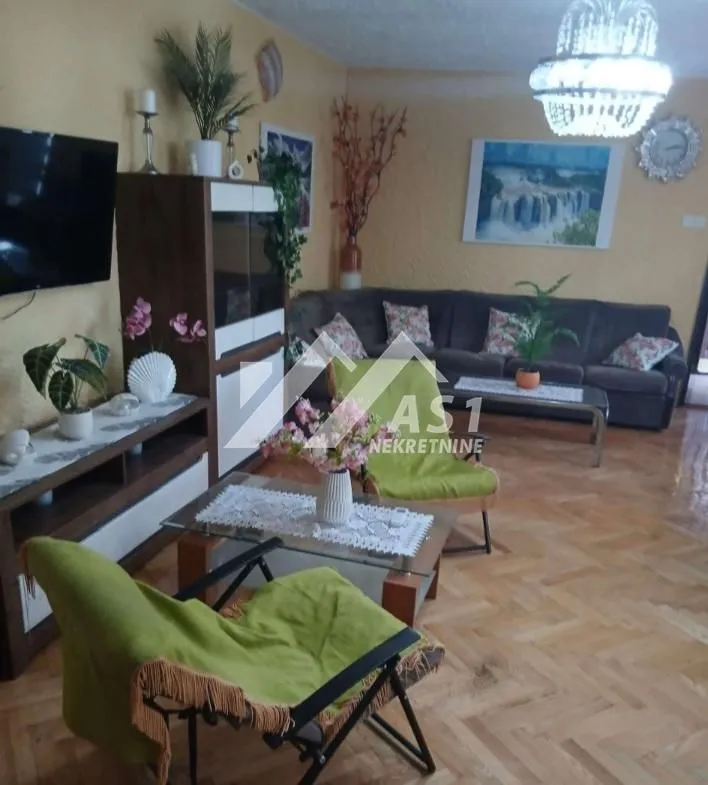 Dnevna soba sa garniturom, TV-om i trpezarijskim stolom.