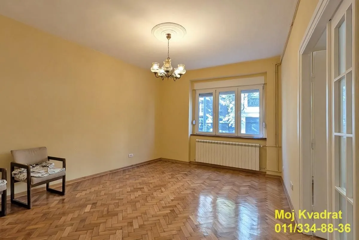 Prazna soba sa parketom, lusterom i prozorom.