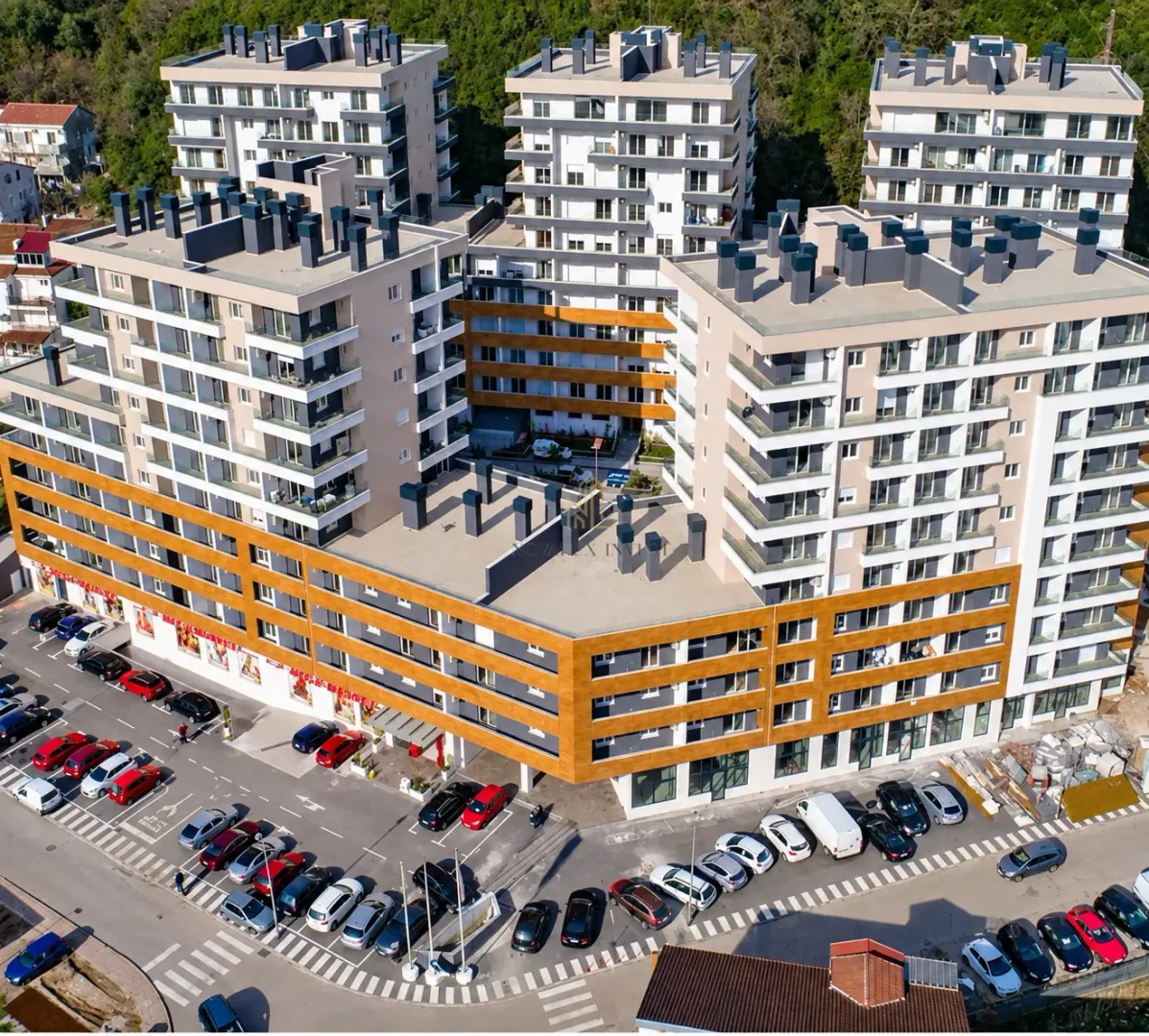 Pogled iz vazduha na kompleks višestambenih zgrada sa parkingom u prizemlju.