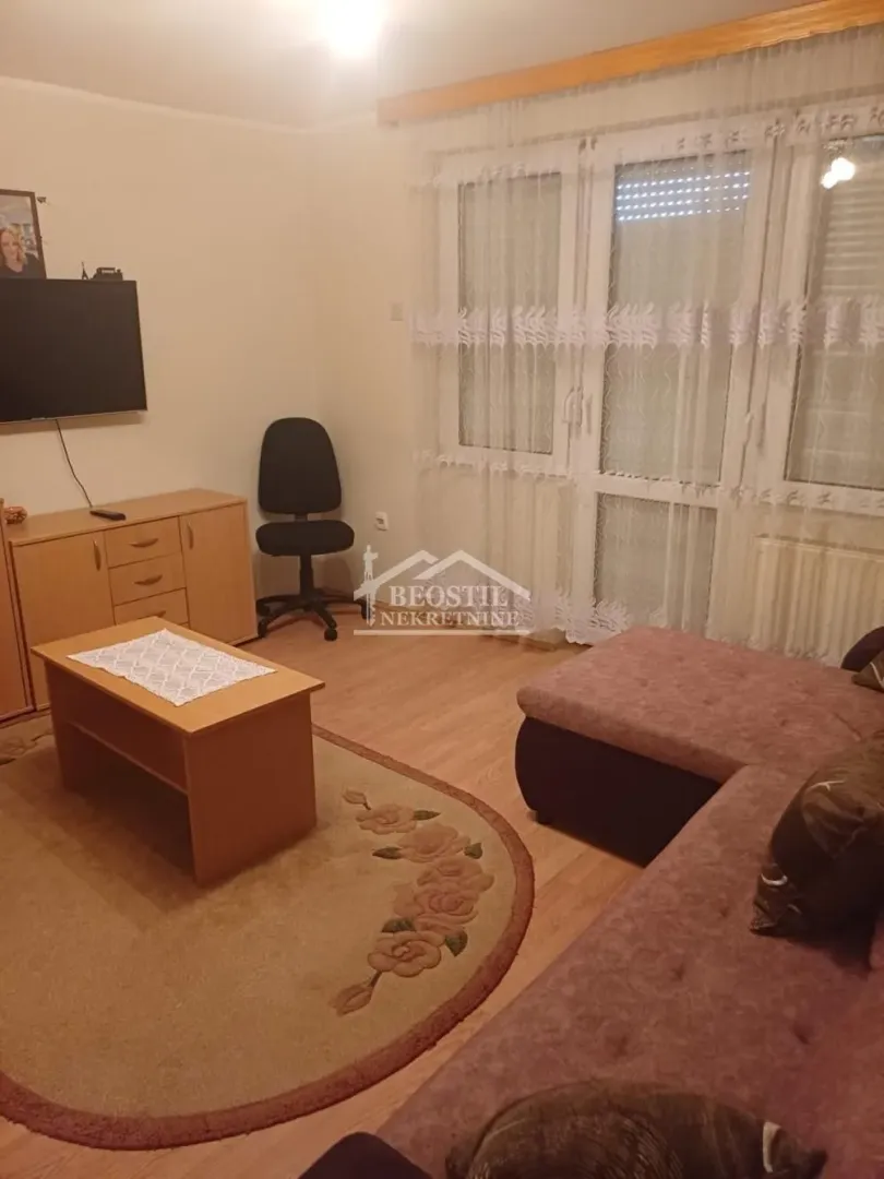 Dnevna soba sa garniturom, stočićem, komodom, televizorom i radnom stolicom.