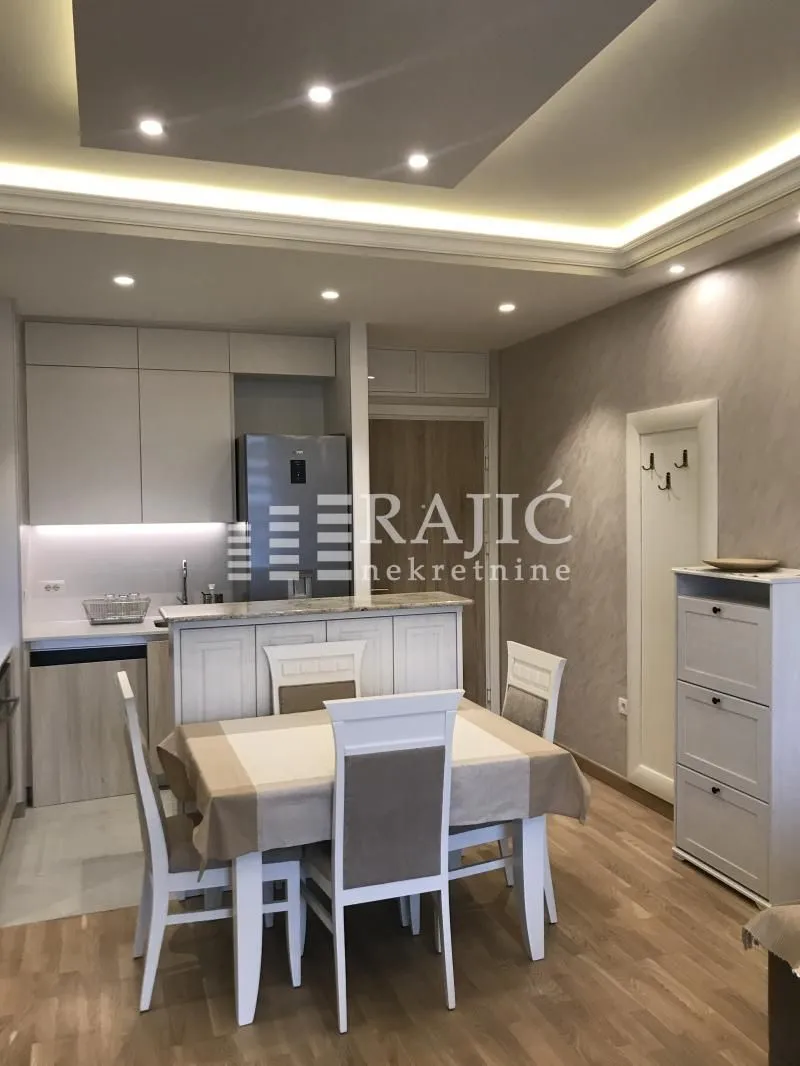 Dining area and kitchen in bright tones with a dropped ceiling and lighting.