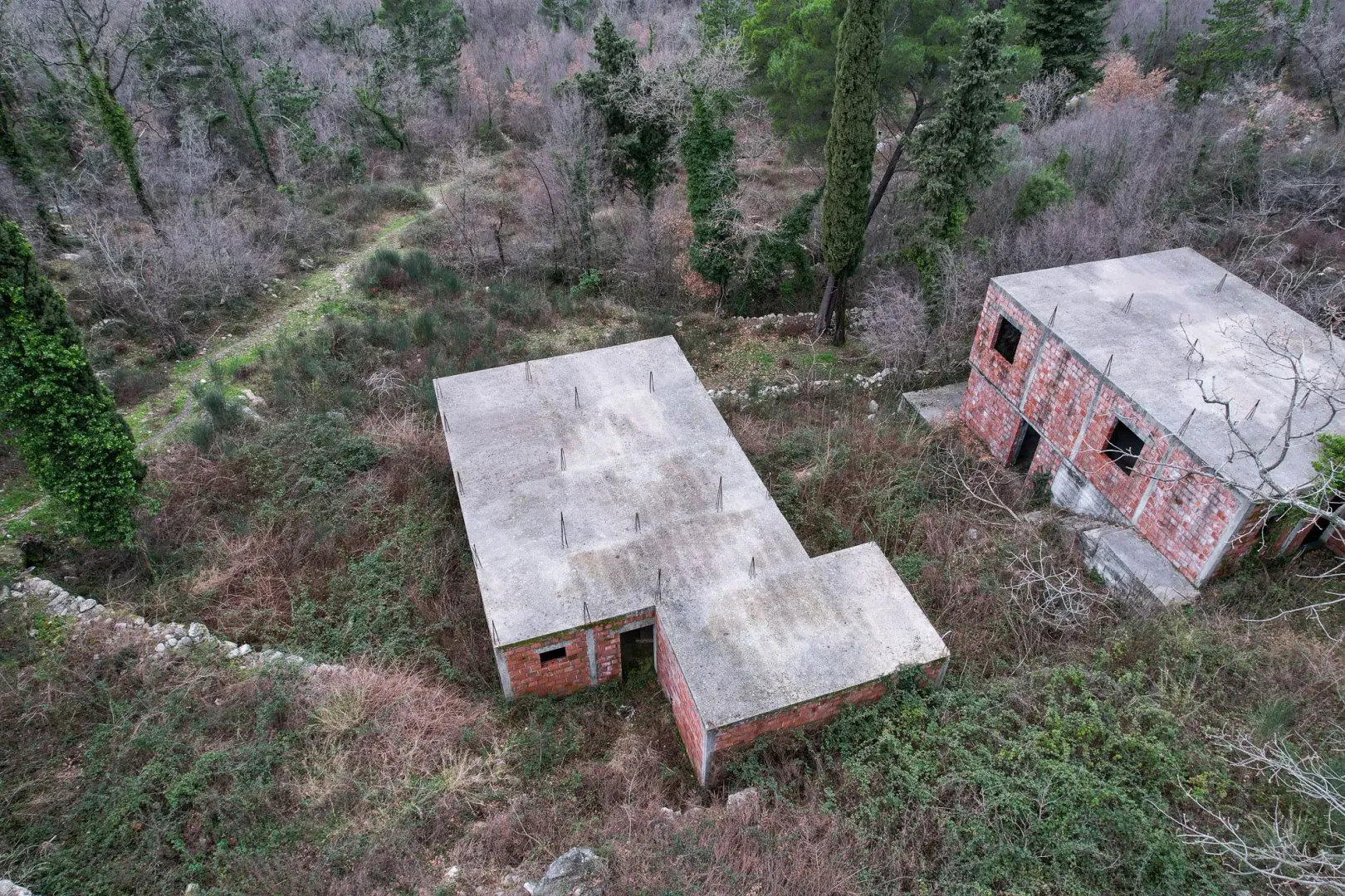 Nedovršeni objekti u sivoj fazi okruženi zelenilom.
