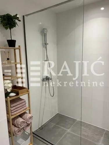 Modern bathroom with a walk-in shower and a wooden shelf with towels.