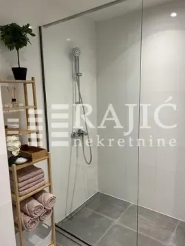 Modern bathroom with a walk-in shower and a wooden shelf with towels. - image 4