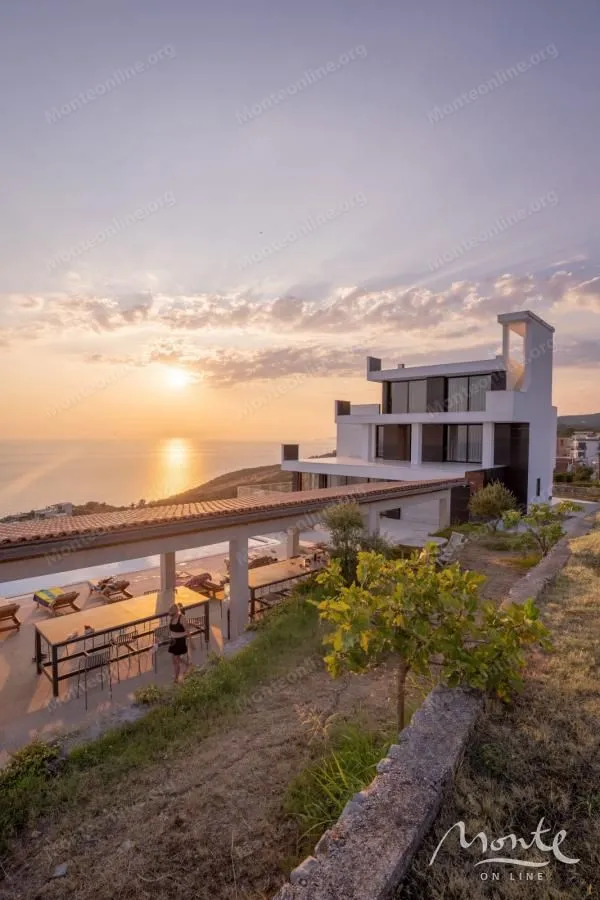 View of the exterior of a luxury villa with a terrace and pool at sunset.