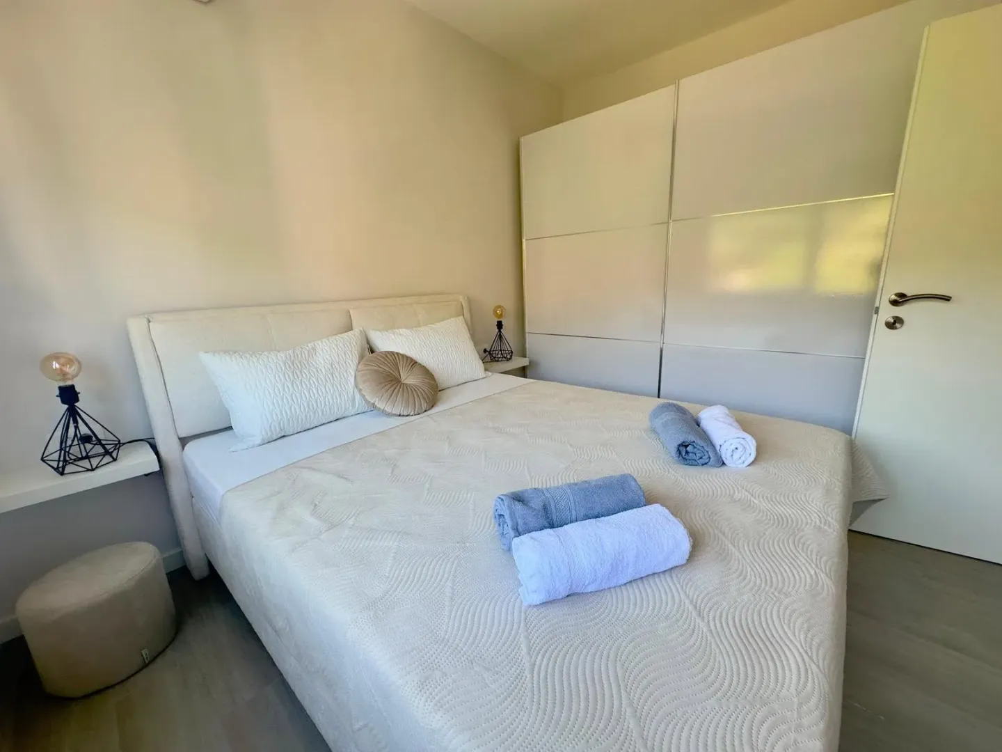 A tidy bedroom with a double bed, wardrobe, and folded towels.
