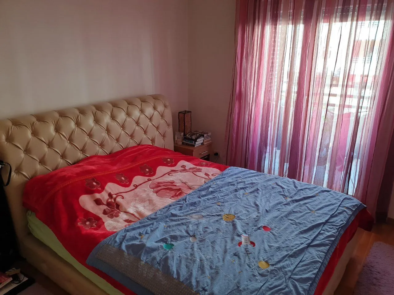 A bedroom featuring a large double bed and pink curtains by the window.