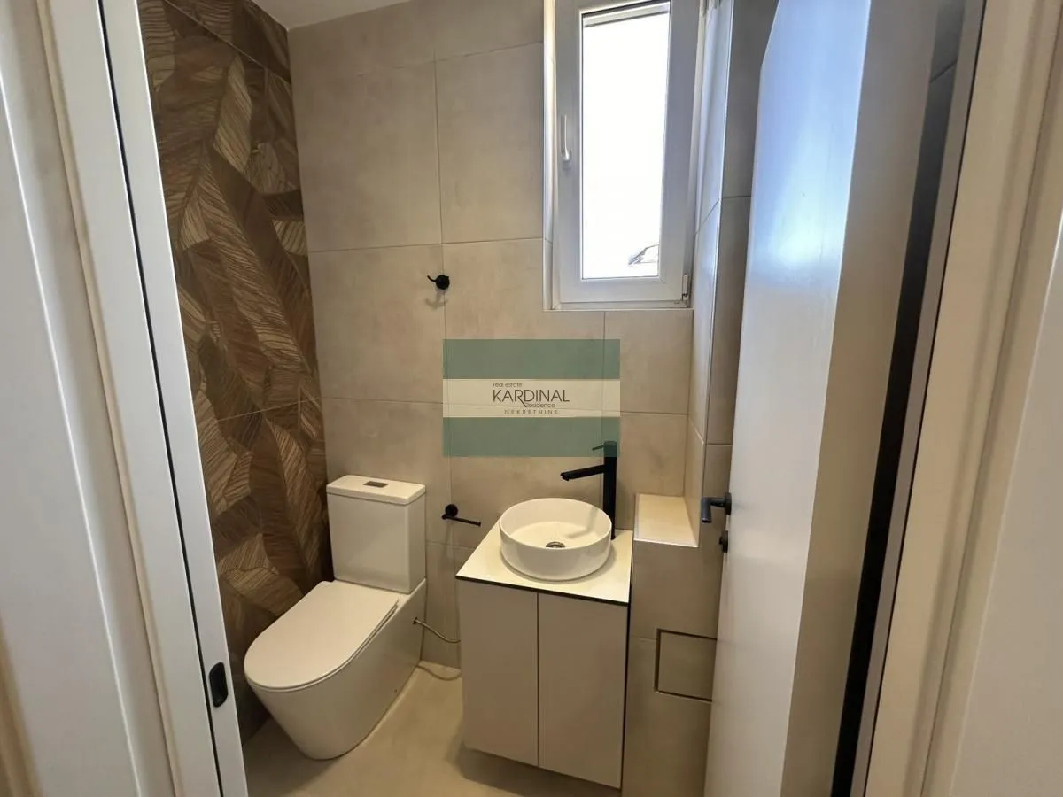 Manje kupatilo sa WC šoljom, umivaonikom i dekorativnim pločicama.