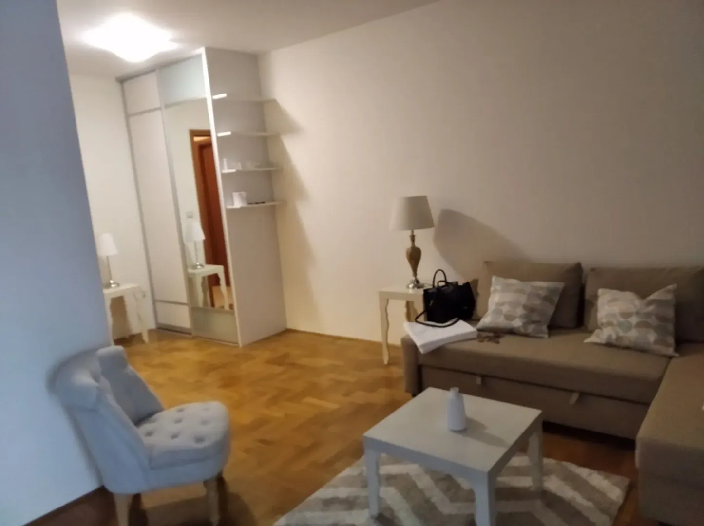 Svijetla dnevna soba sa ugaonom garniturom i foteljom.