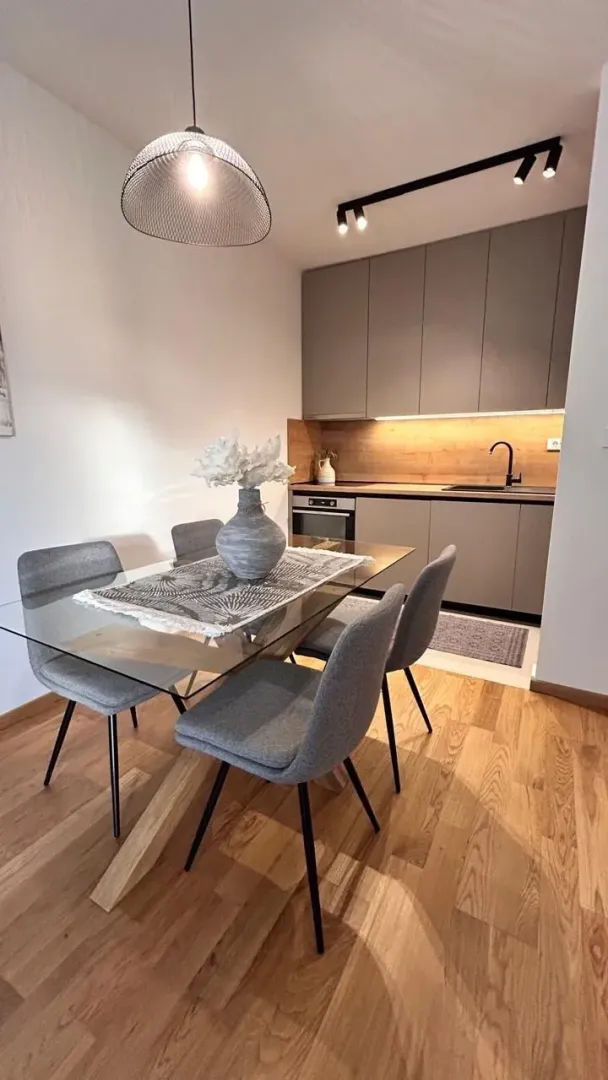 Modern dining area with a glass table and a kitchen with grey cabinets in the background.