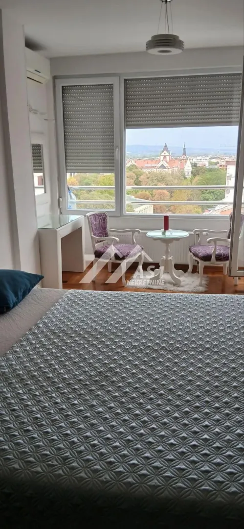 Nameštena spavaća soba sa krevetom i malim kutkom za sedenje pored prozora.