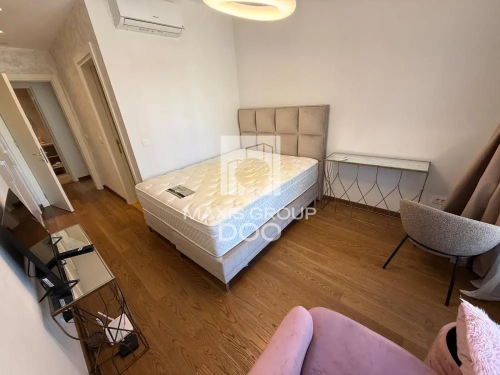 Nameštena spavaća soba sa bračnim krevetom, foteljom i TV komodom.