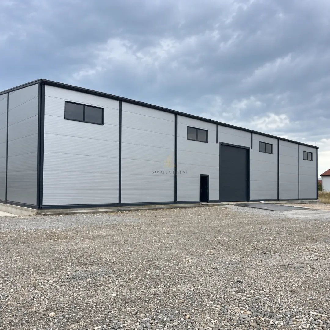 Exterior view of a newly built industrial building with large doors and a gravel yard.