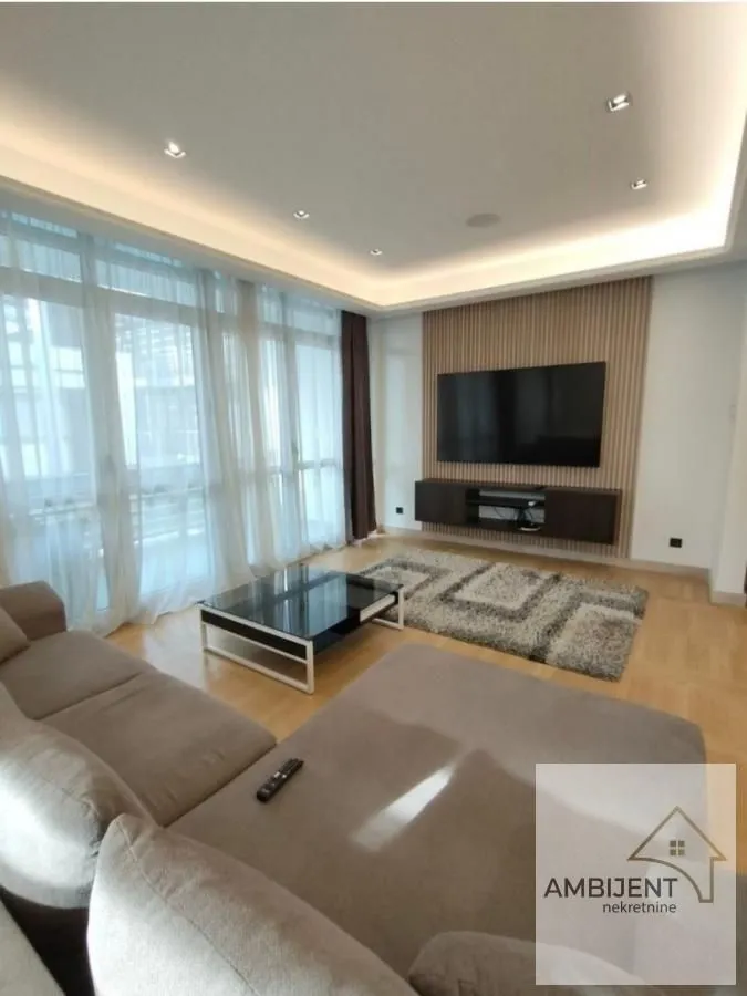 Living room with a sofa, TV, and large windows with light curtains.