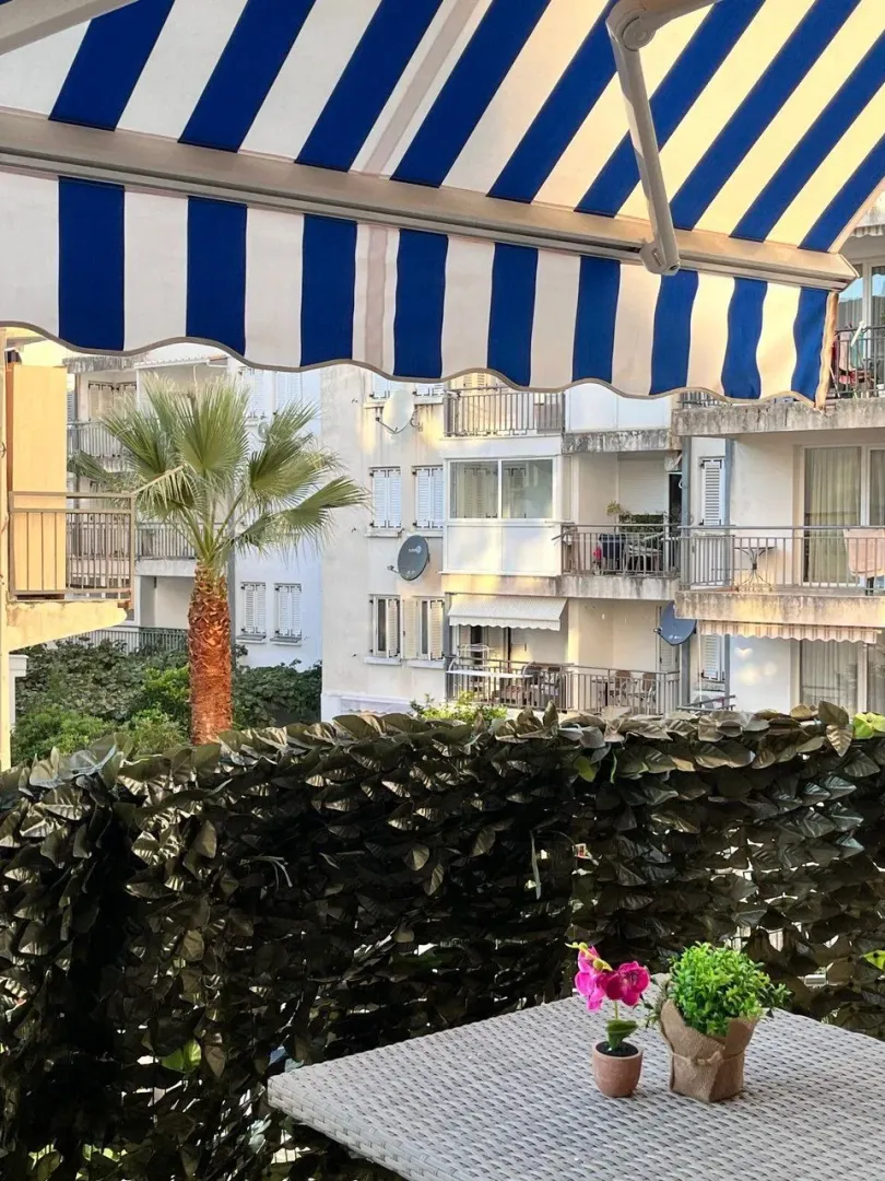 Namješten balkon sa tendom i pogledom na okolne zgrade i zelenilo.