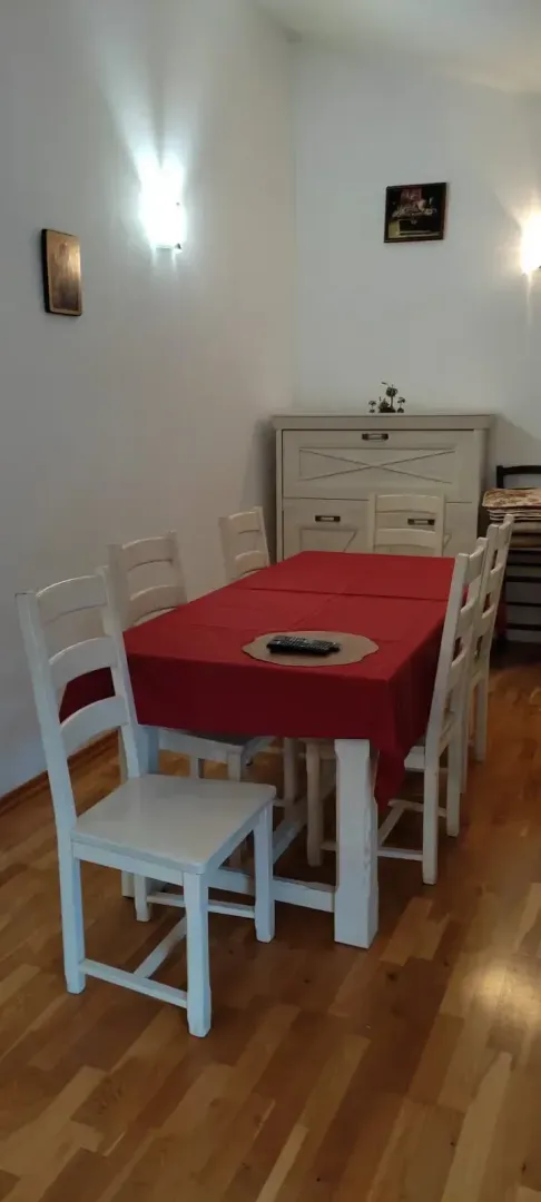 Dining table with white chairs and a red tablecloth.