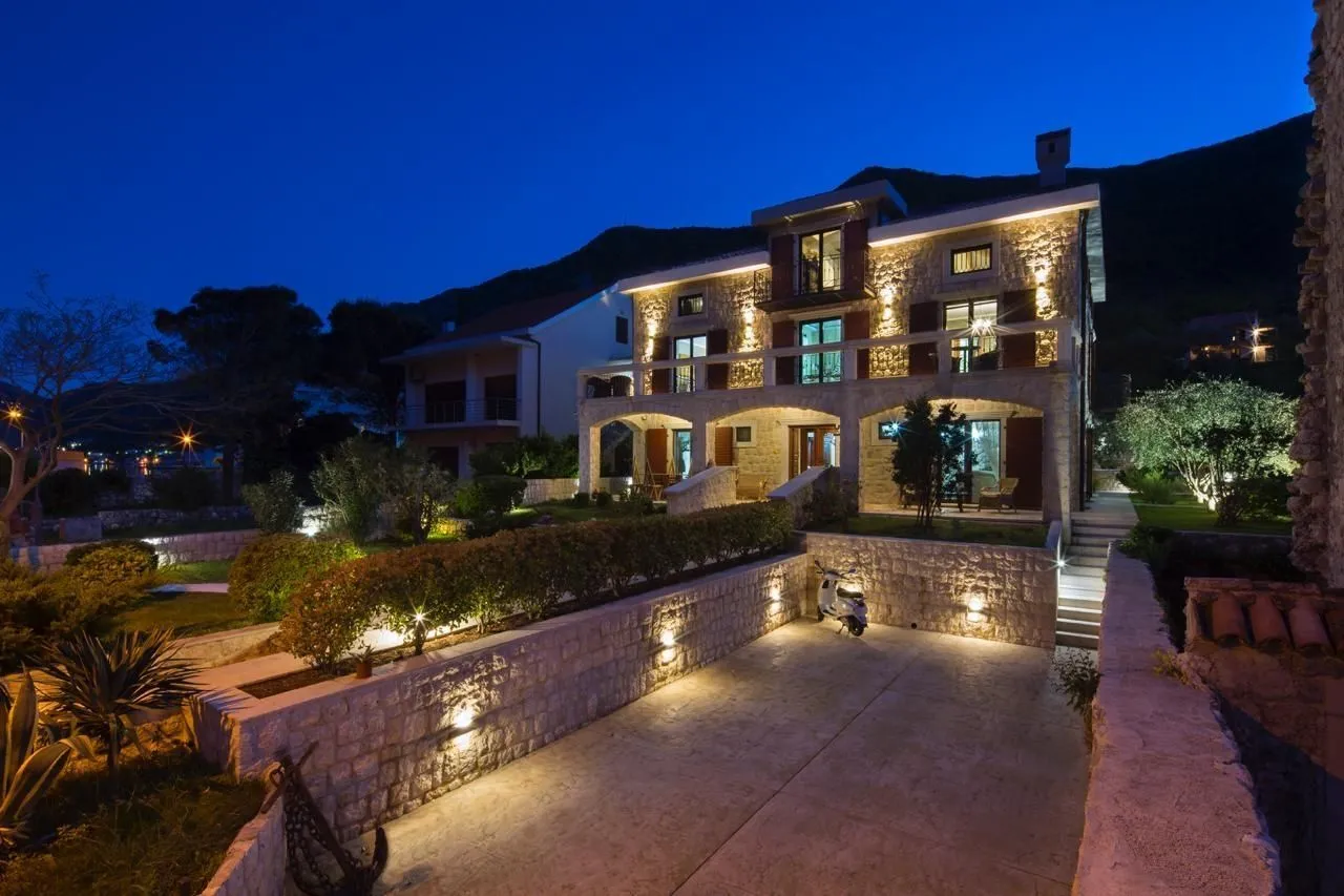 Stone house with illuminated yard and parking at night.