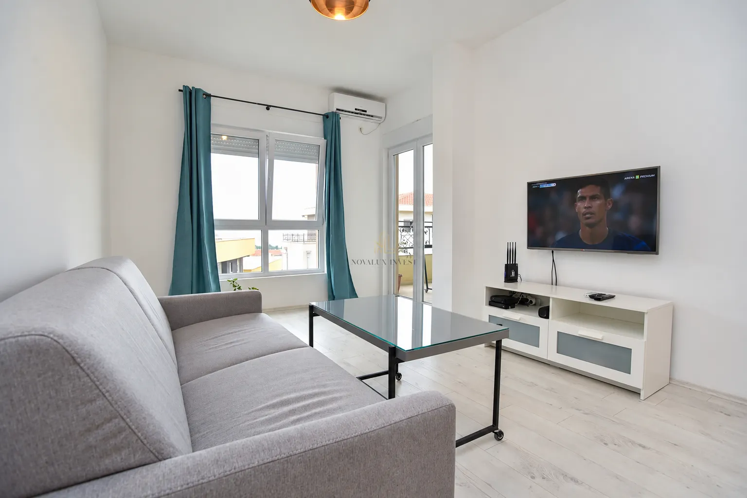 Living room with a gray sofa, glass coffee table, and a wall-mounted TV.