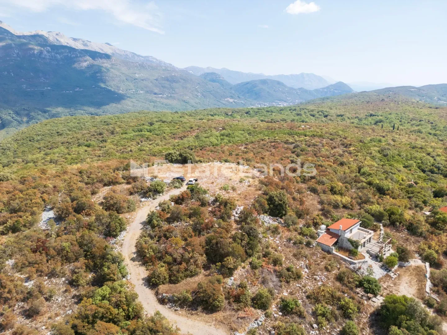 Pogled iz vazduha na imanje sa kućom i planinskim pejzažem u pozadini.