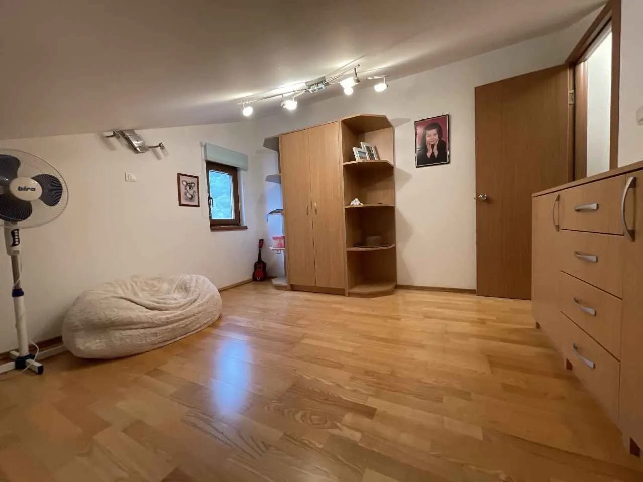 Namještena spavaća soba sa drvenim podom, ormarom i komodom.