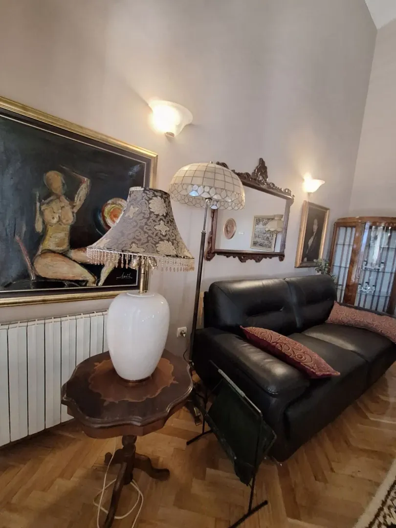Living room with a leather sofa, a small table with a lamp, and artworks on the wall.