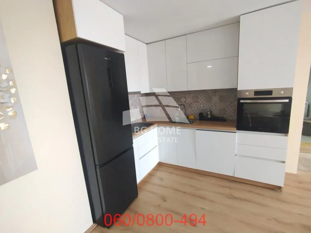 Moderna bela kuhinja sa ugrađenim aparatima i crnim frižiderom.