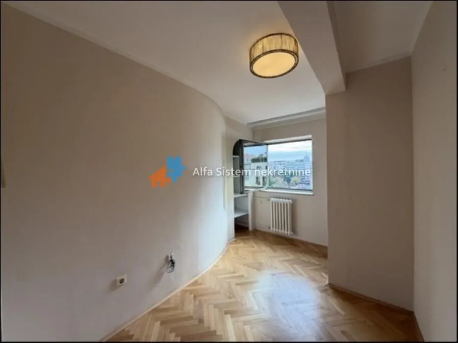 Empty room with hardwood parquet flooring and a window.