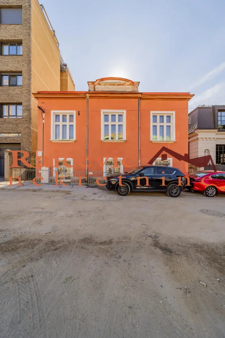 View of the facade of an orange house with parked cars in front.