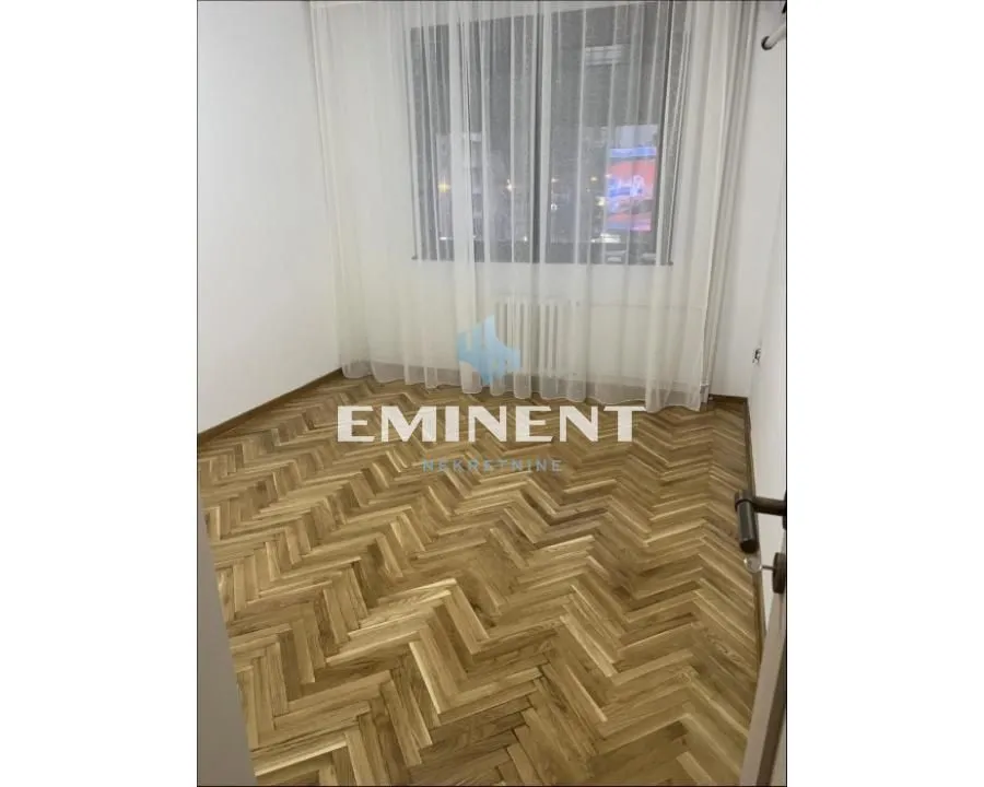 Prazna soba sa parketom i belim zavesama na prozoru.