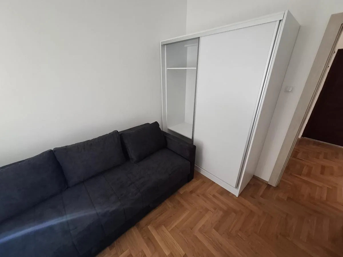 Manja spavaća soba sa tamnim kaučem i belim garderoberom.