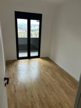 Prazna soba sa parketom i izlazom na balkon sa pogledom na grad. - image 3