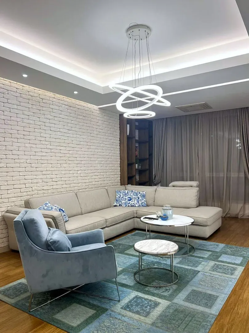 Dnevna soba sa ugaonom garniturom, foteljom i modernim lusterom.