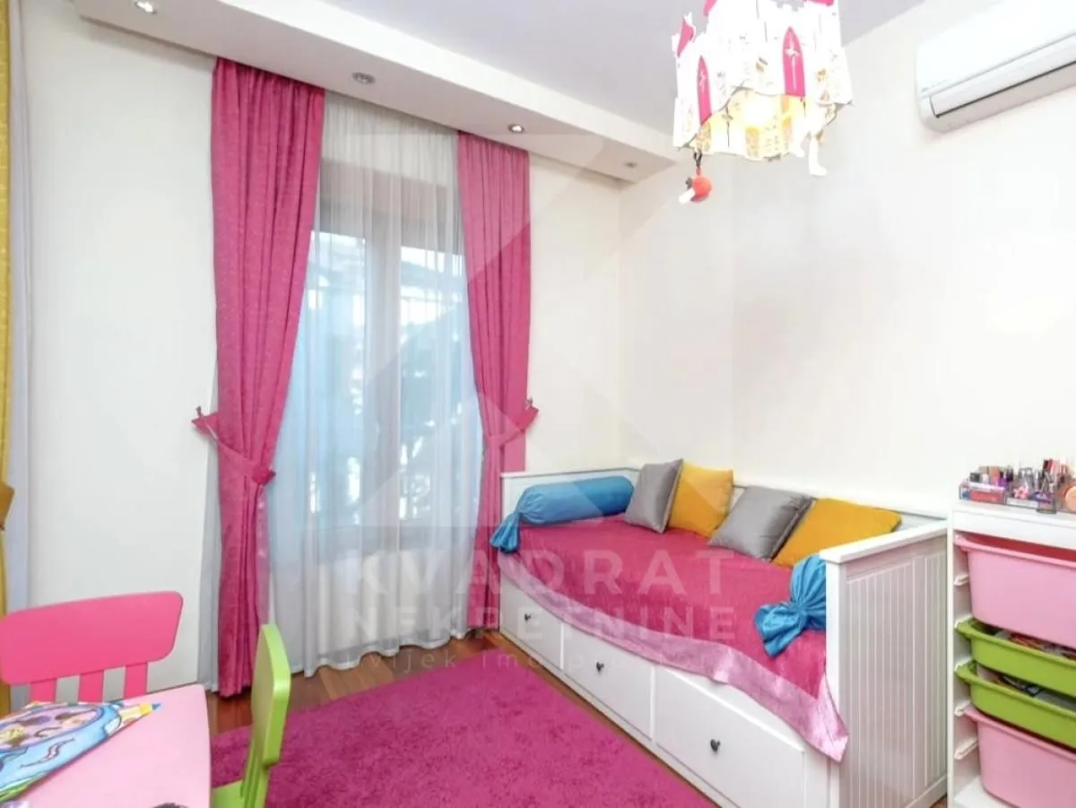 Dječja soba sa krevetom, roze zavjesama i tepihom.