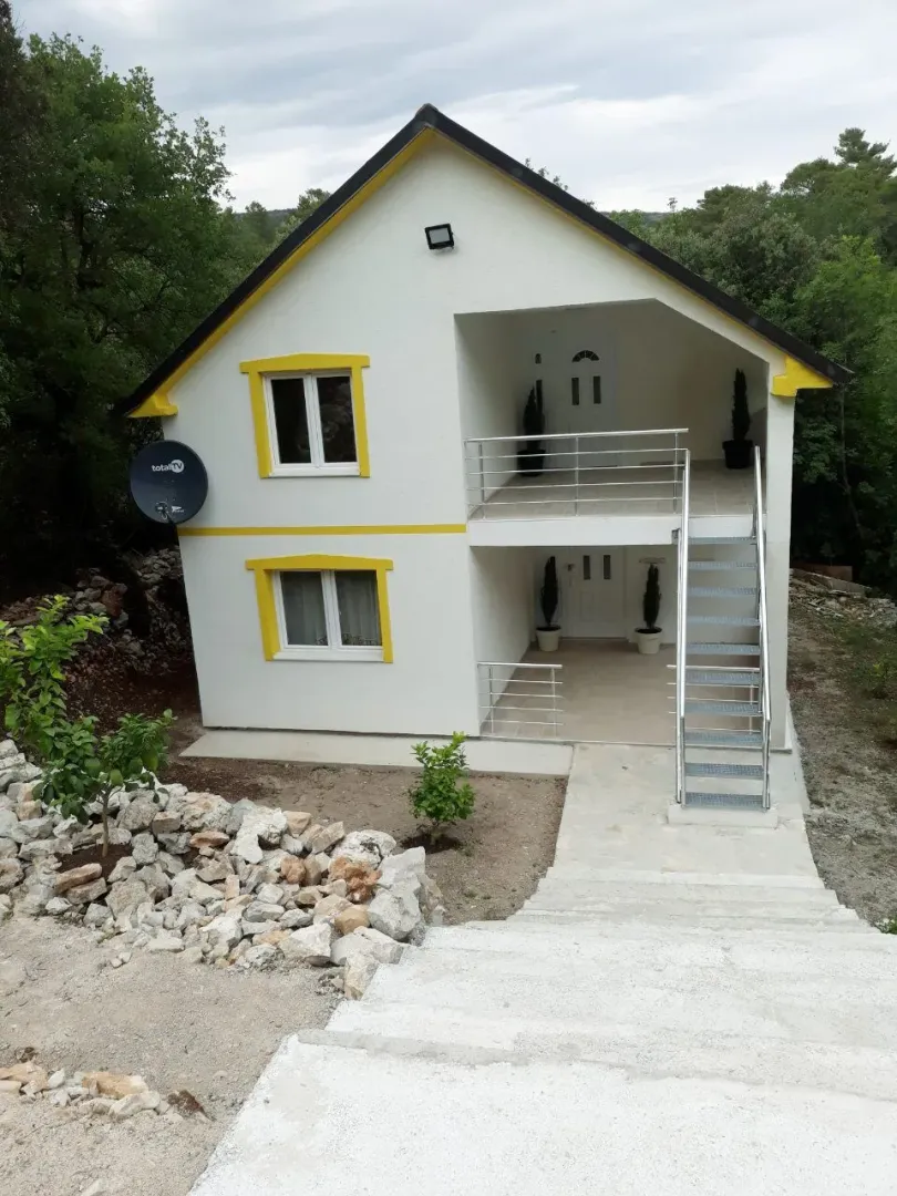 Dvospratna kuća sa bijelom fasadom i vanjskim stepenicama.
