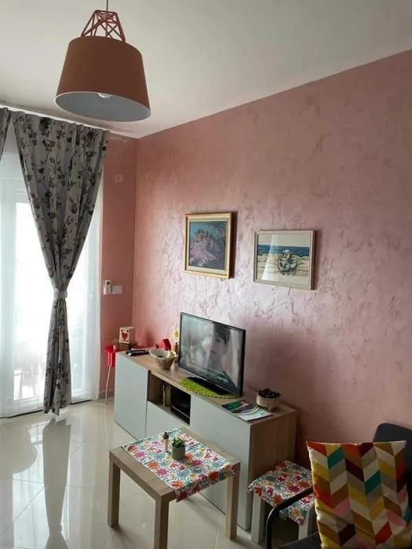 Dnevna soba sa roze zidom, TV komodom i izlazom na terasu.