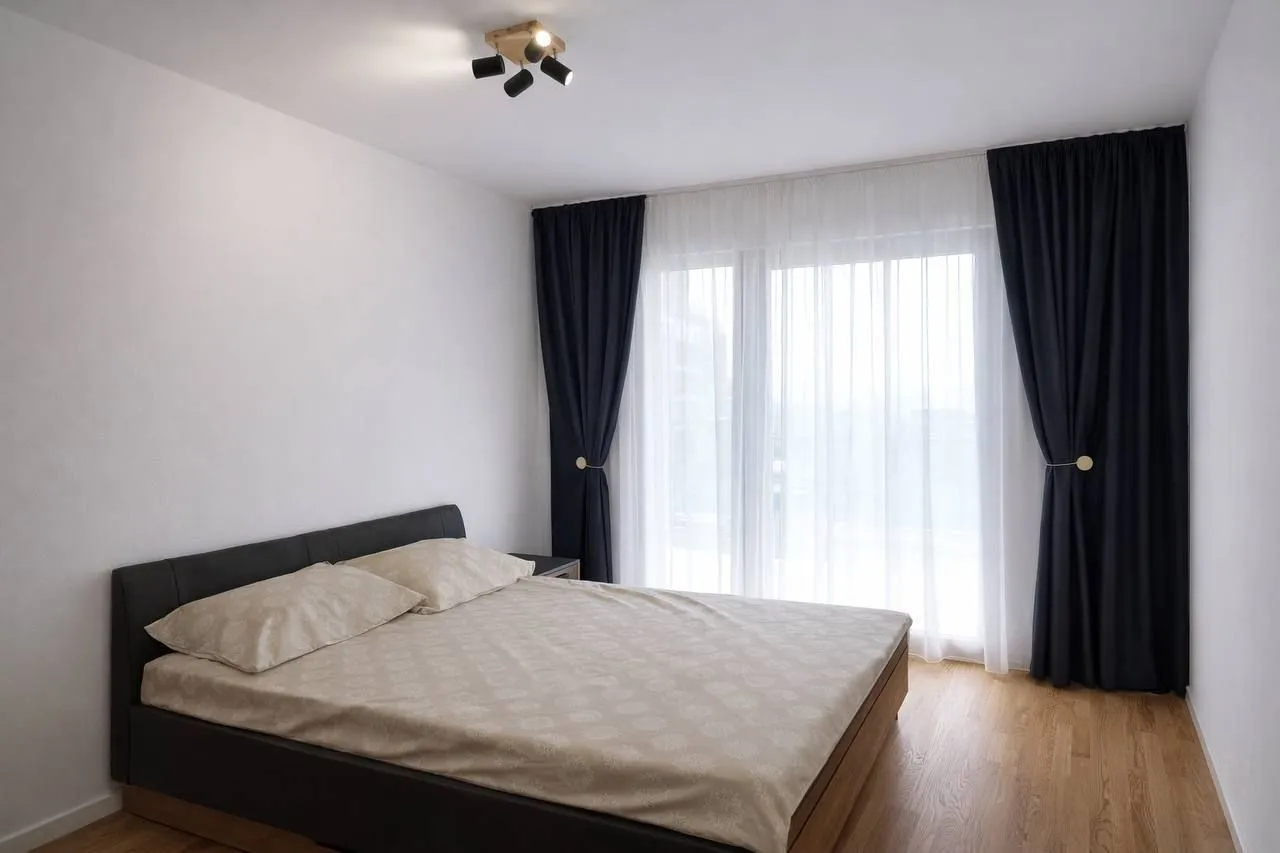 Svijetla spavaća soba sa bračnim krevetom i tamnim zavjesama.